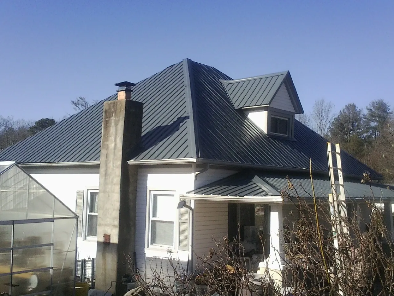 Dark blue standing seam metal roof on a white farmhouse with dormer — Slate & Tile Roof Repair by Roofing Brothers in Thayne
