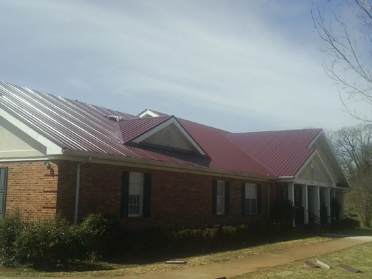 Red metal roof with gabled entries on a long brick building, from a Hail Damage Roof Repair job in Thayne