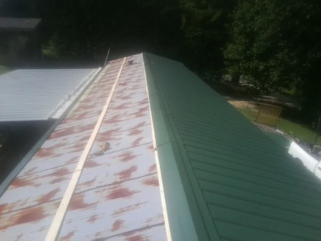 Old rusted panels beside newly installed green metal roofing — Wind Damage Roof Repair by Roofing Brothers in Thayne
