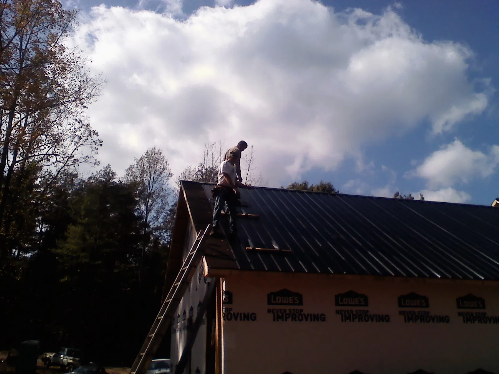 Roofer fastening dark metal panels high against a cloudy sky, from a Roof Inspection job in Thayne