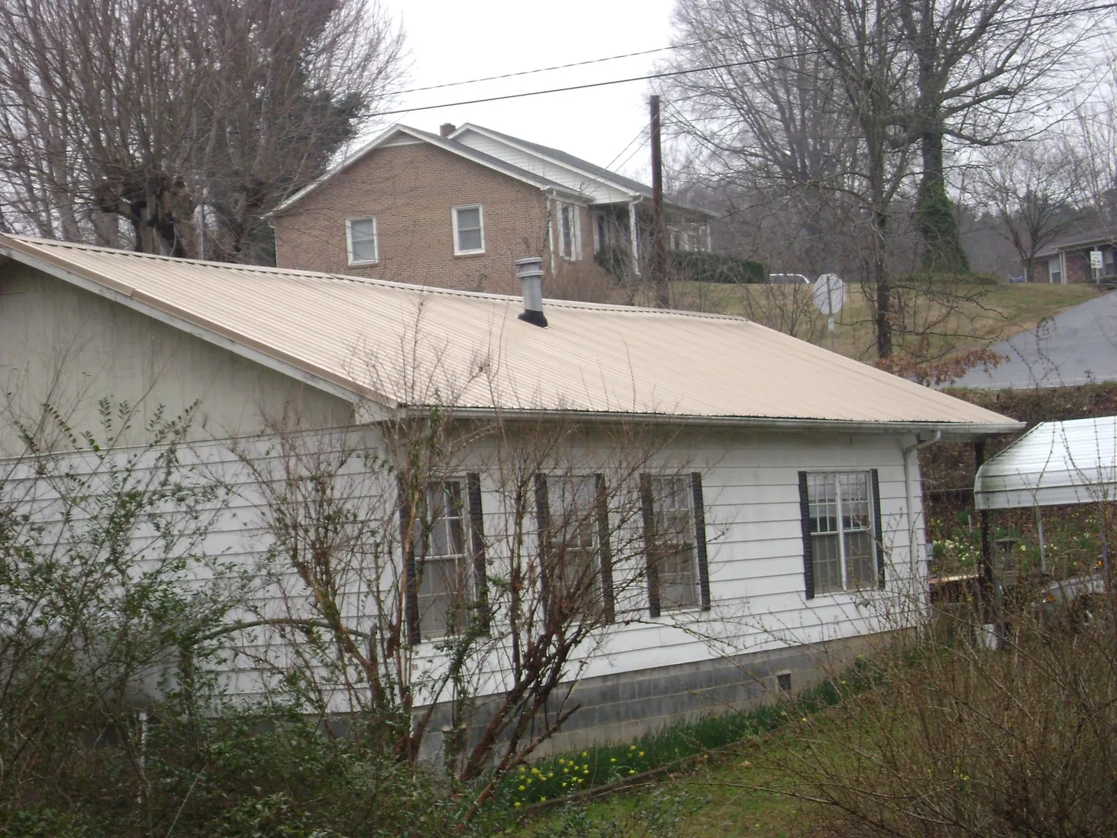 Tan metal roof on a white sided house set into a hillside — Commercial Roofing by Roofing Brothers in Thayne